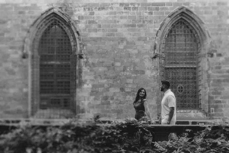 Laughing couple strolls hand in hand past gothic arches during a couples & engagements photoshoot in an old city courtyard.