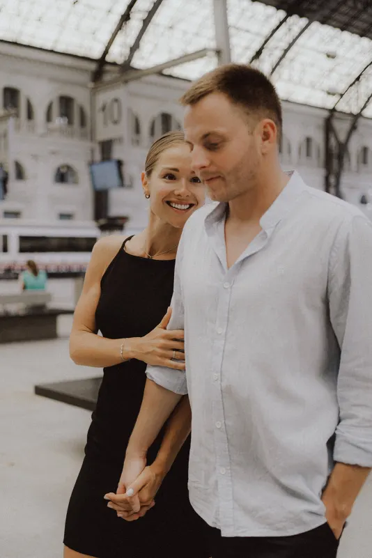 Laughing woman holds her partner’s arm as they walk together during a couples & engagements session at a train station.