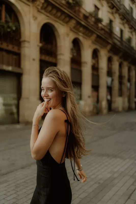 Laughing woman in a black dress strolls past historic arches, captured during a Vacation Portraits photoshoot in Europe.