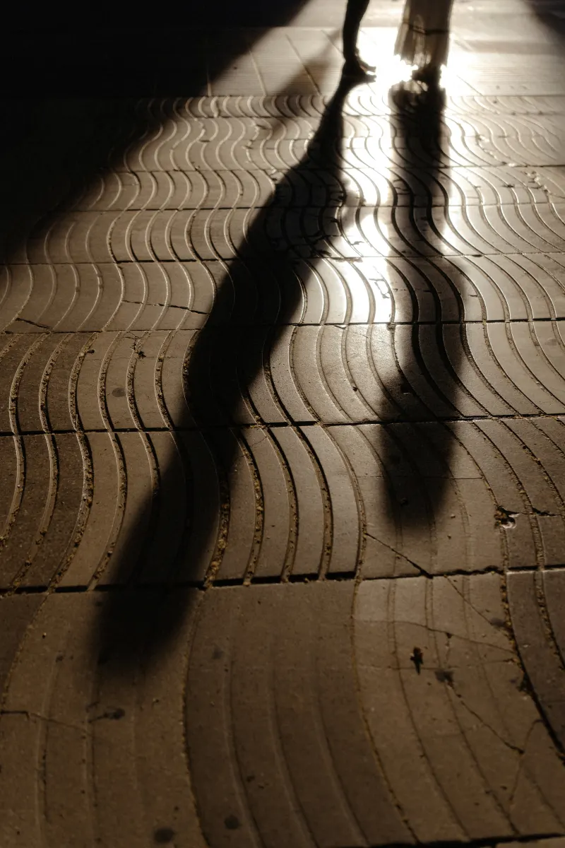 Long shadows of a couple standing close together on a sunlit patterned walkway during an engagement photoshoot.