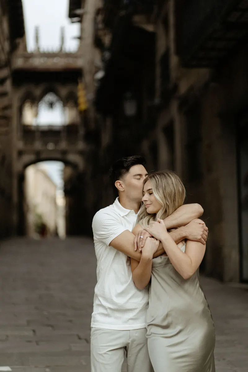 Man embraces his partner and kisses her head in Barcelona’s Gothic Quarter during a Vacation Portraits photoshoot.