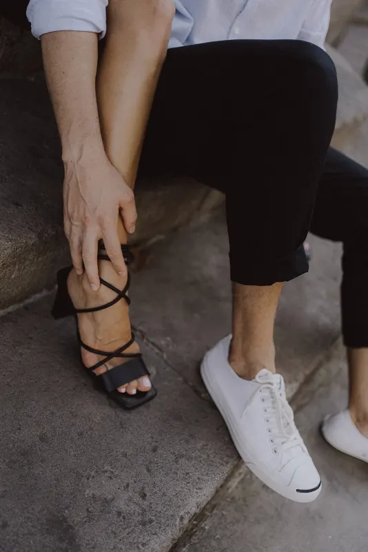 Man gently holds his partner’s ankle as they sit close on stone steps, captured during a couples & engagements session.