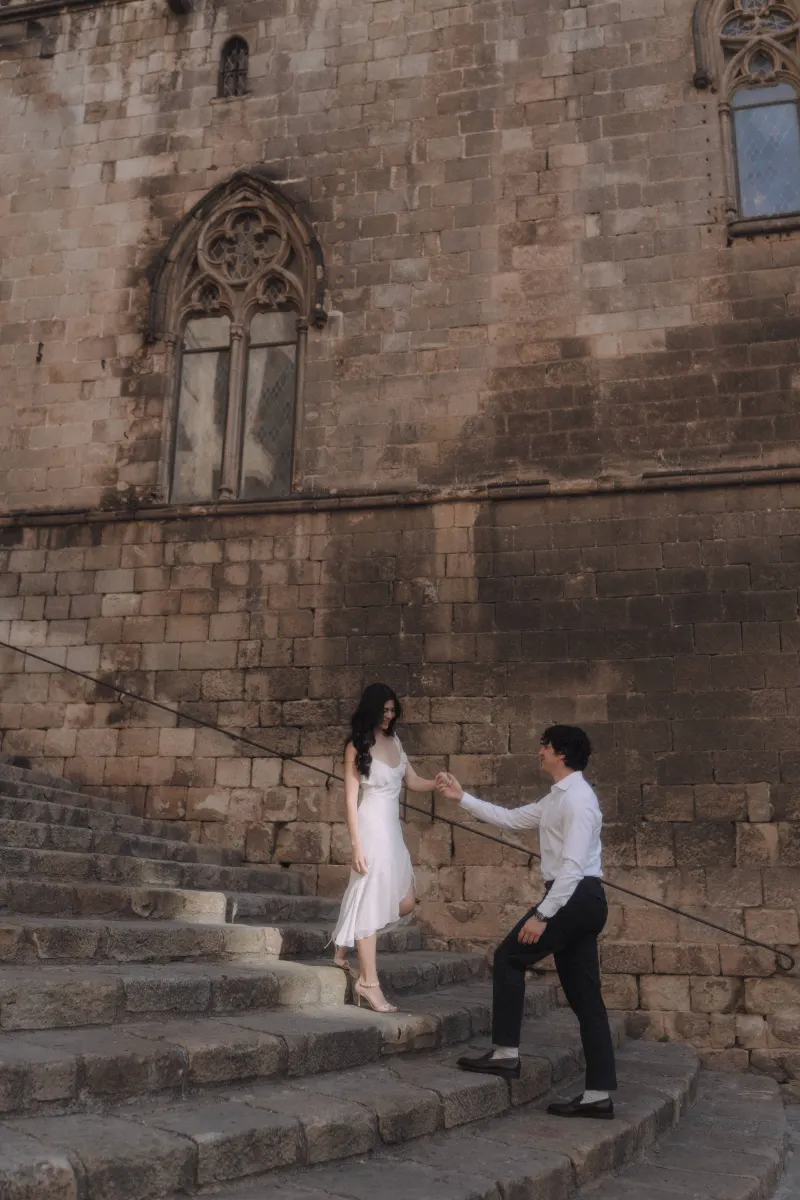 Man helps his partner down historic stone steps, sharing a tender moment during a couples & engagements photoshoot.