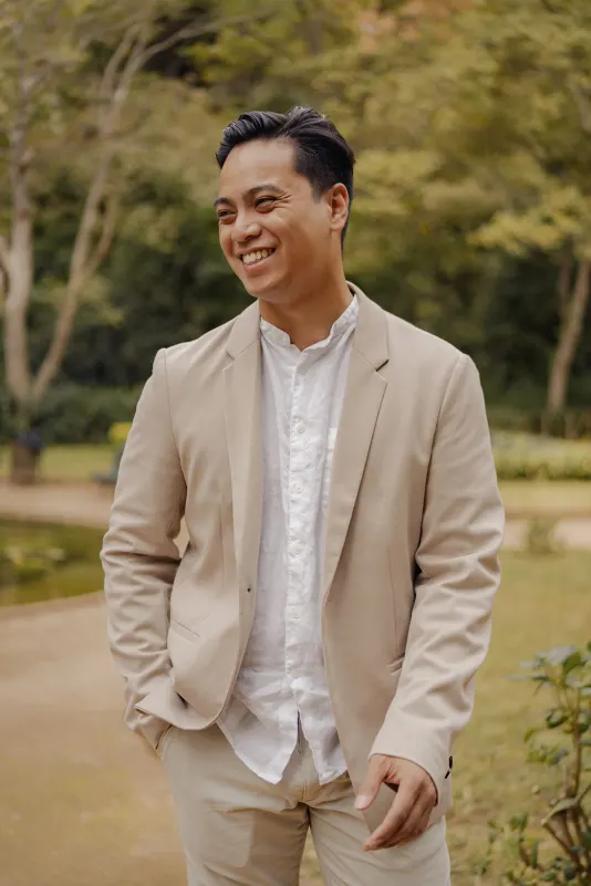 Man in a light suit smiling warmly during a couples photoshoot in a peaceful garden setting.