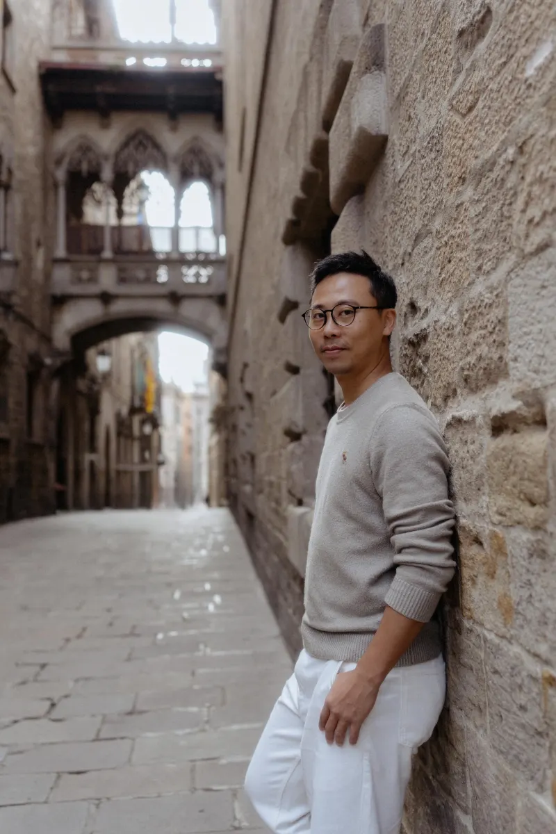 Man in casual clothes leans against a stone wall, smiling during a Vacation Portraits photoshoot in Barcelona’s Gothic Quarte