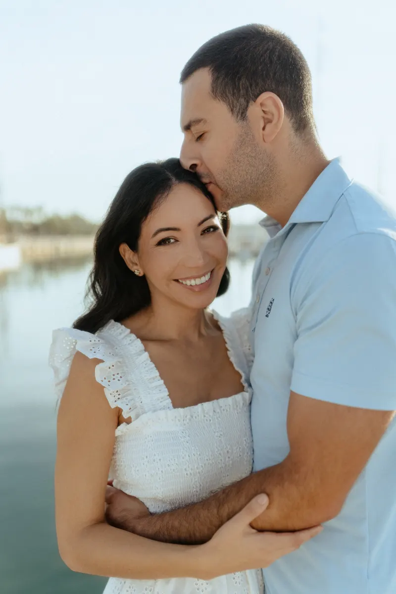 Man kisses his partner’s forehead as she smiles, captured during a couples & engagements photoshoot by the marina.