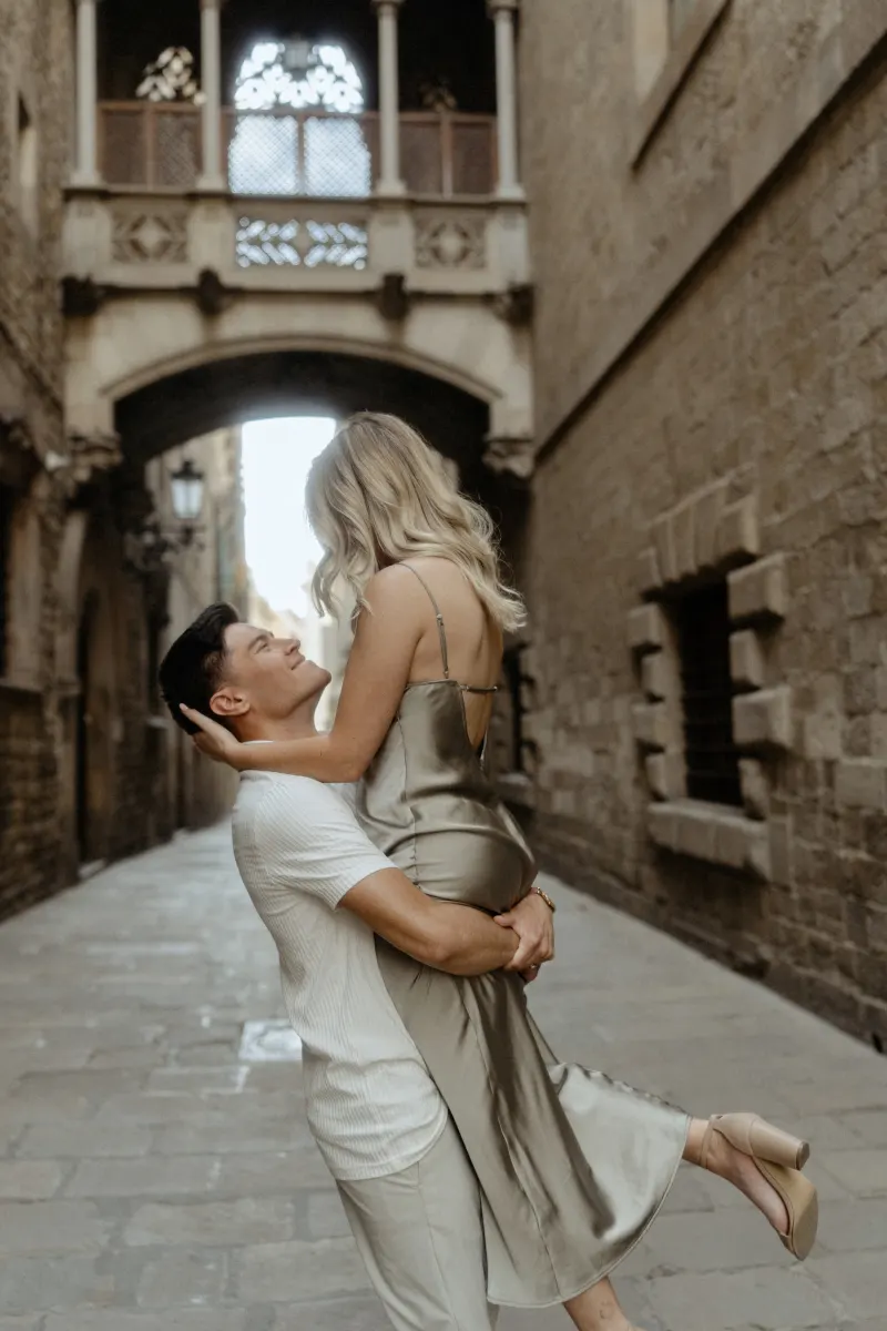 Man lifts his partner in a joyful embrace beneath Barcelona’s Gothic bridge during a Vacation Portraits session.