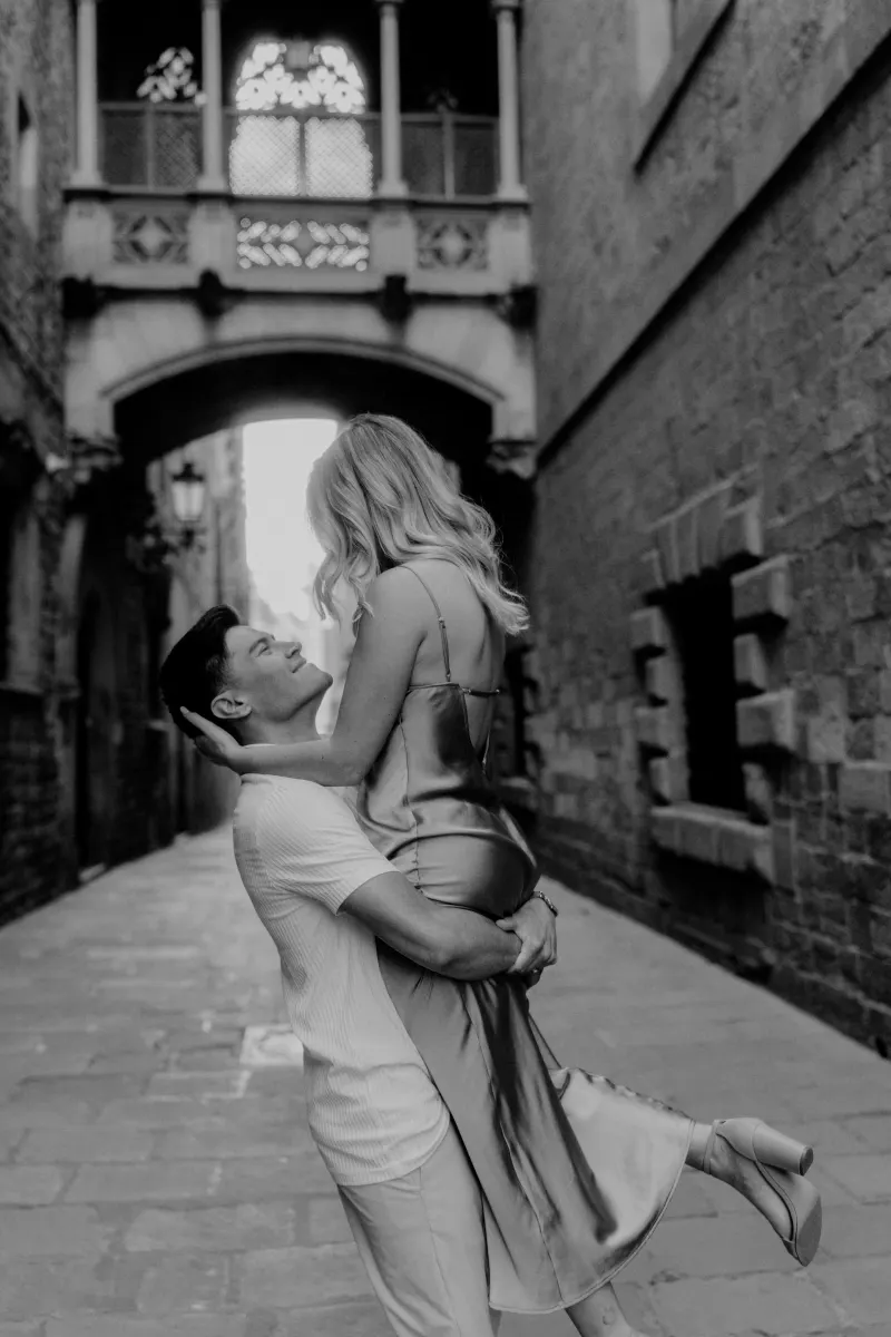 Man lifts his partner in a joyful embrace beneath Barcelona’s iconic Gothic bridge during a Vacation Portraits session.