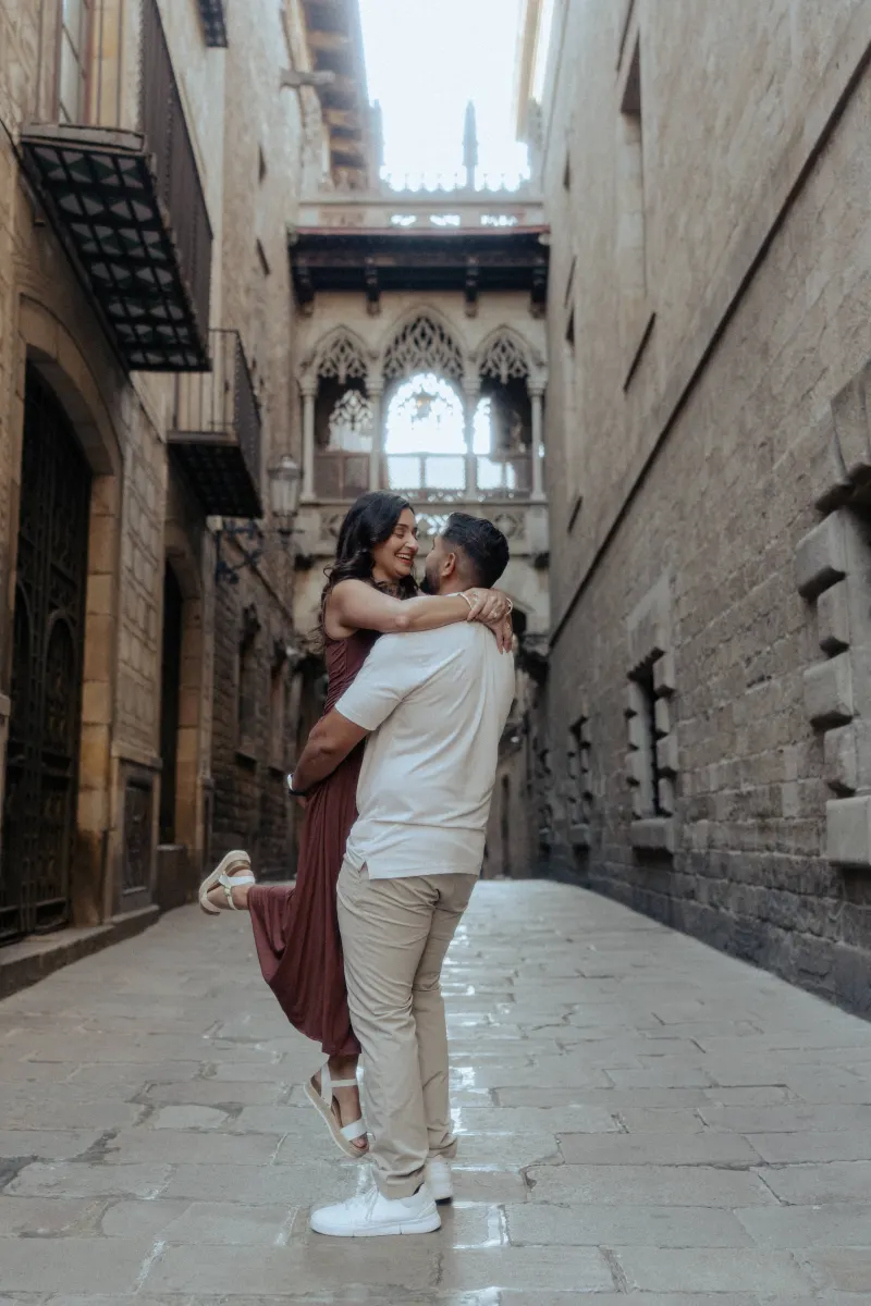 Man lifts his partner in a joyful embrace during a couples & engagements photoshoot in a historic European alleyway.