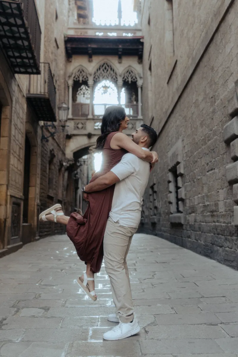 Man lifts his partner in a joyful embrace during a couples & engagements photoshoot in a romantic historic alley.