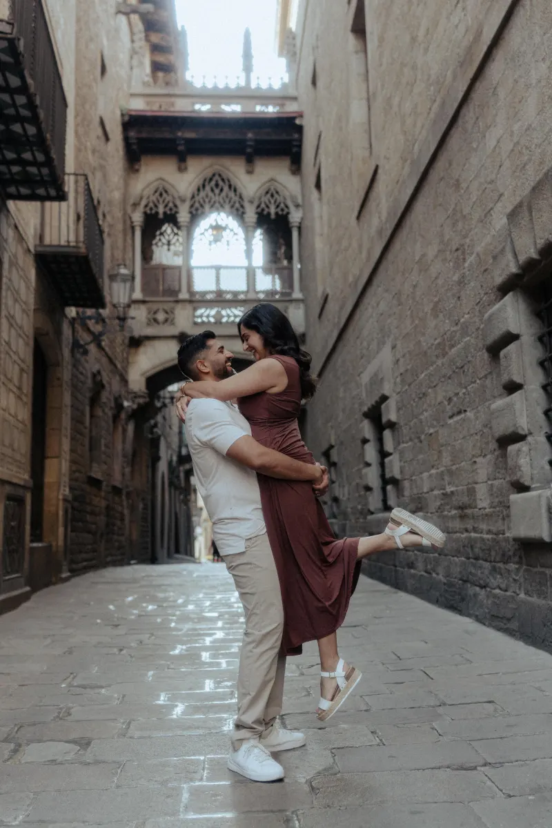 Man lifts his partner in a joyful embrace during a couples & engagements photoshoot in a romantic old city alley.