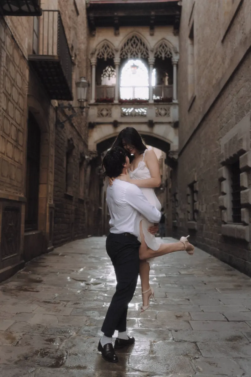 Man lifts his partner in a joyful embrace on a cobblestone street during a couples & engagements photoshoot in Barcelona.