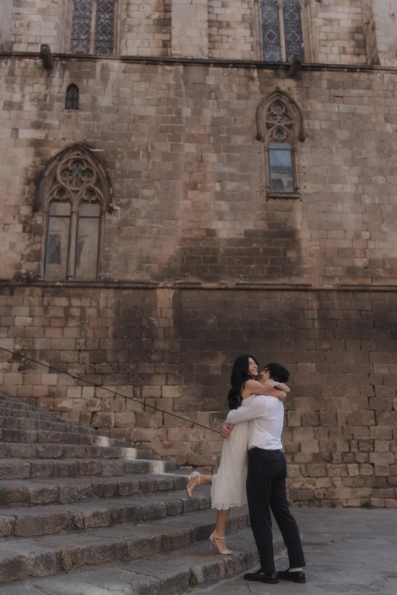 Man lifts his partner in a joyful embrace on historic stone steps during a couples & engagements photoshoot in Barcelona.