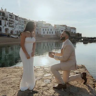 Man proposes on a sunlit seaside pier, capturing a joyful surprise proposal photoshoot by the water.