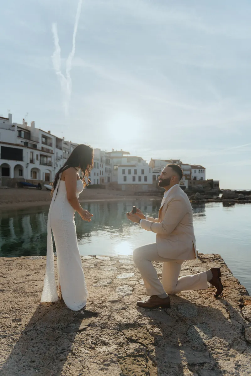Man proposes to his partner at sunset by the water in a romantic surprise proposal photoshoot in a coastal village.