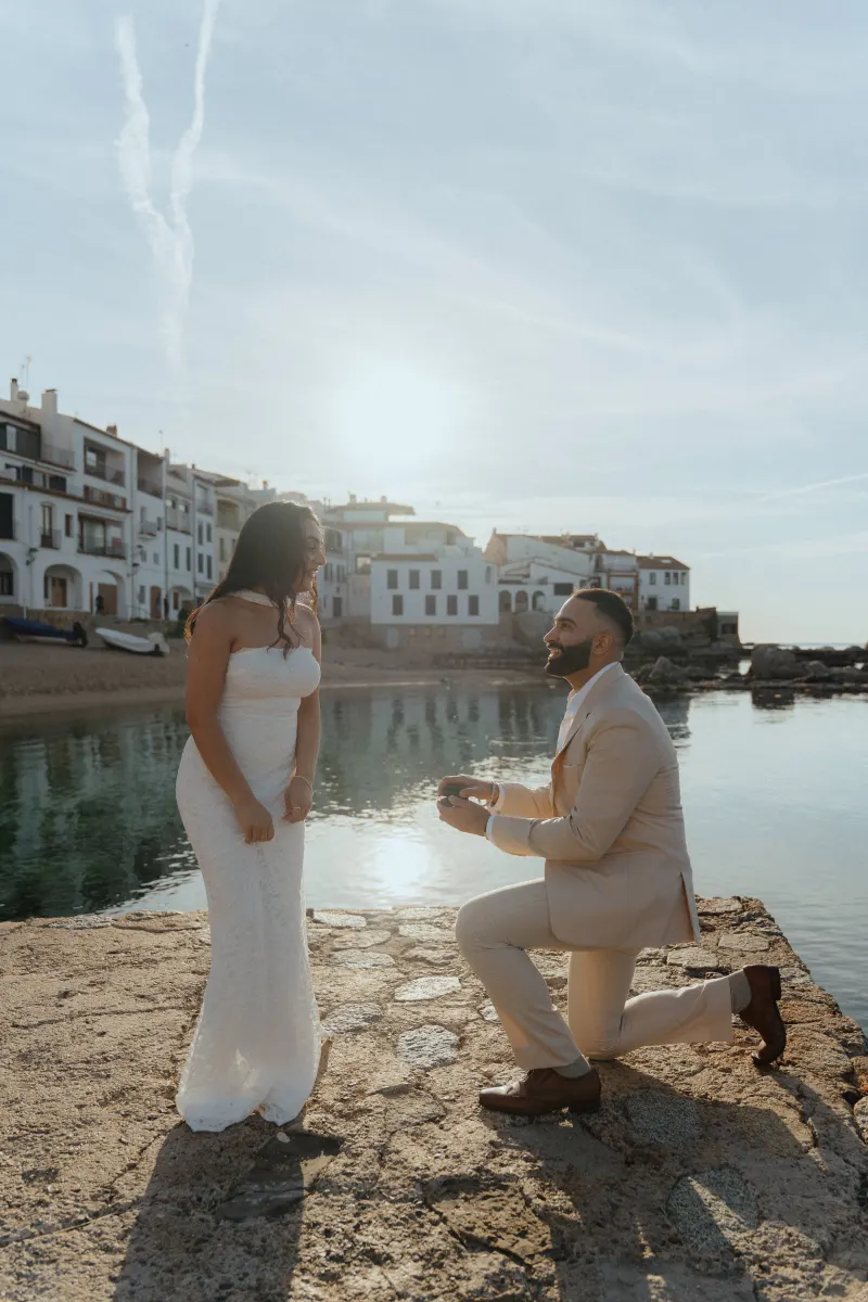 Man proposes to his partner by the water at sunset, capturing a joyful surprise proposal photoshoot moment.