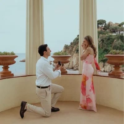 Man proposing to his surprised partner by the sea, capturing a joyful moment during a surprise proposal photoshoot.