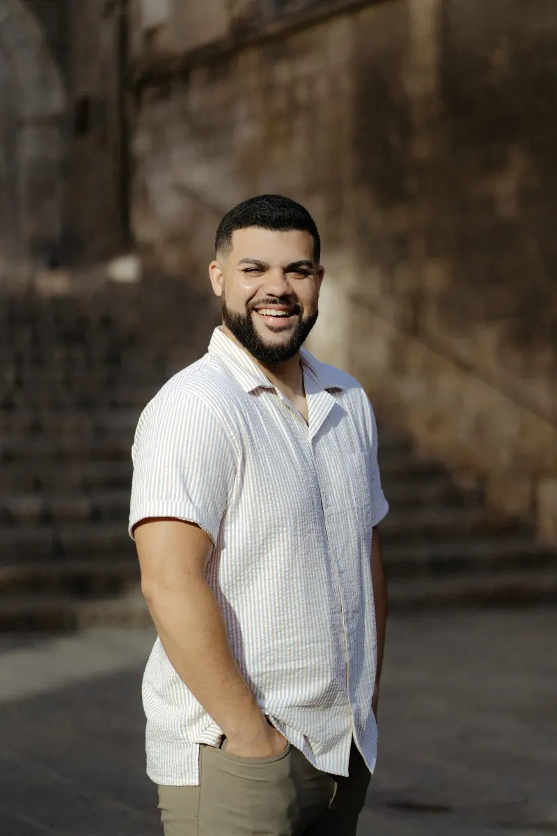 Man smiles warmly in golden sunlight, standing on historic stone steps during a couples & engagements photoshoot.