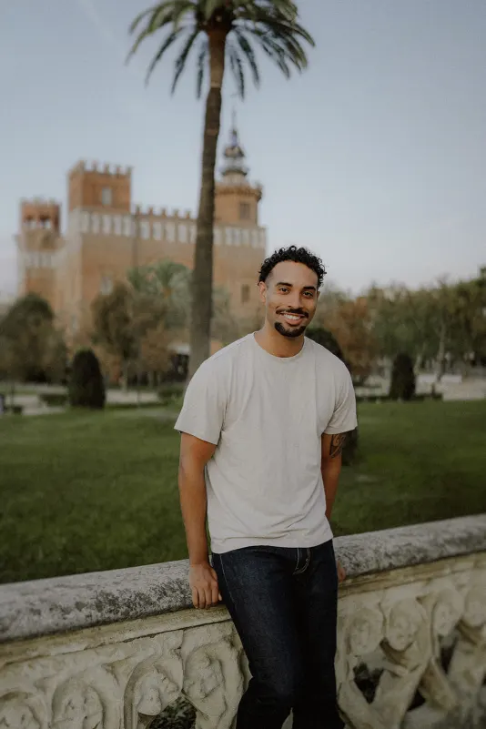Man smiling and leaning on a stone railing in a historic park, captured during a couples & engagements photoshoot session.