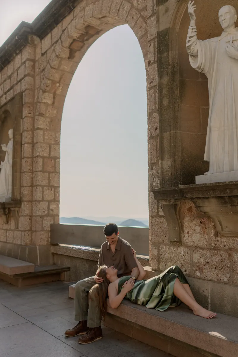 Megan rests across Tim's lap on a stone bench beneath an arch.