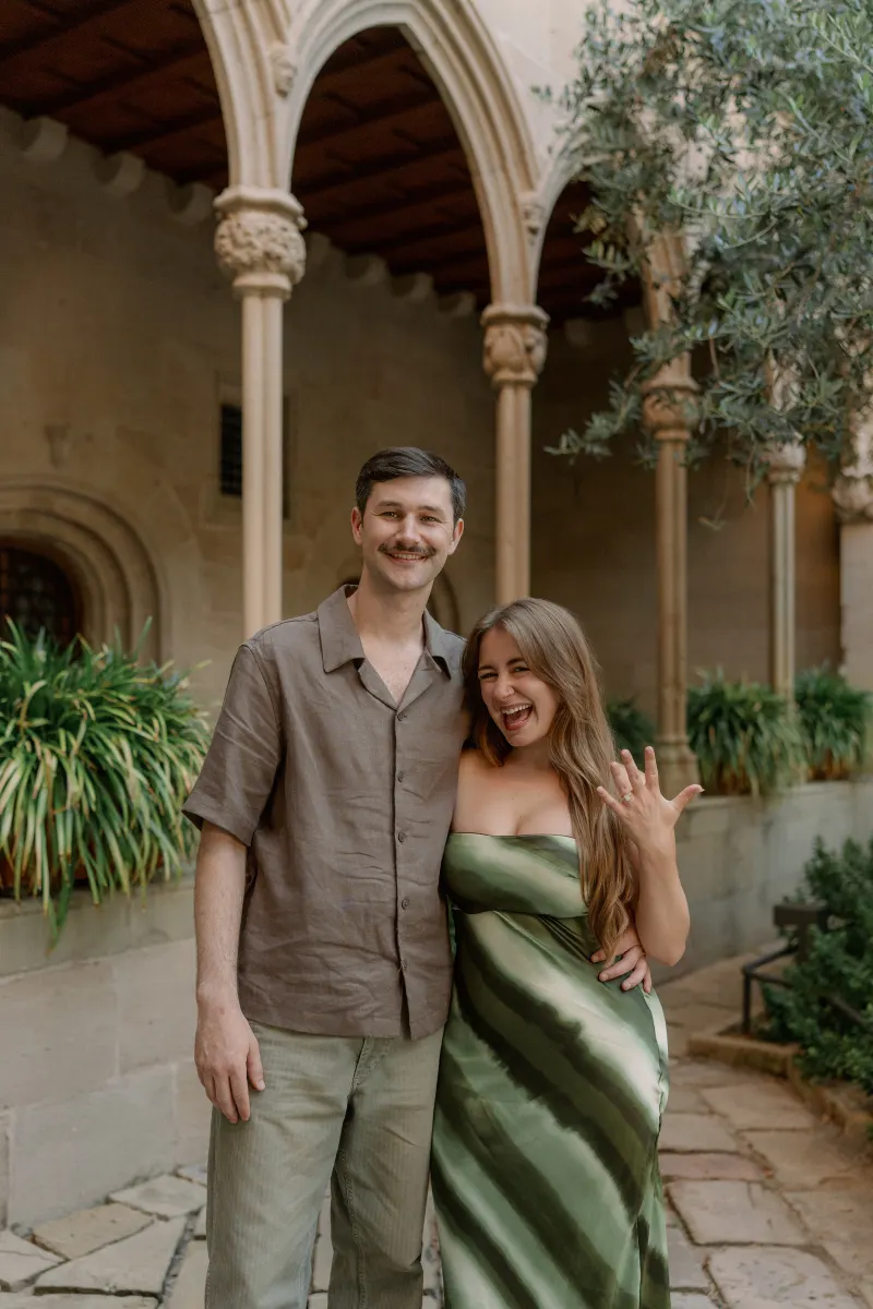 Megan shows her engagement ring while standing beside Tim in the cloister.
