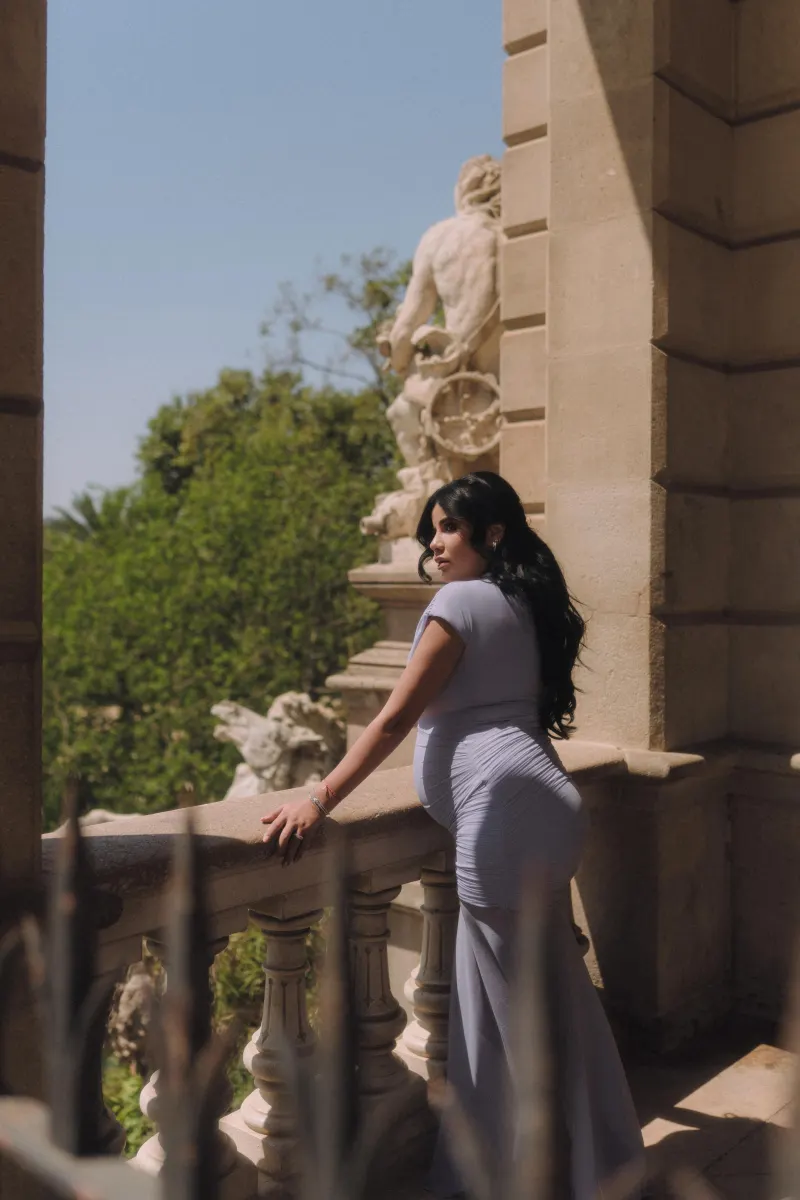 Mom-to-be in a lavender dress leans on a sunlit balcony, Vacation Portraits session in Barcelona.