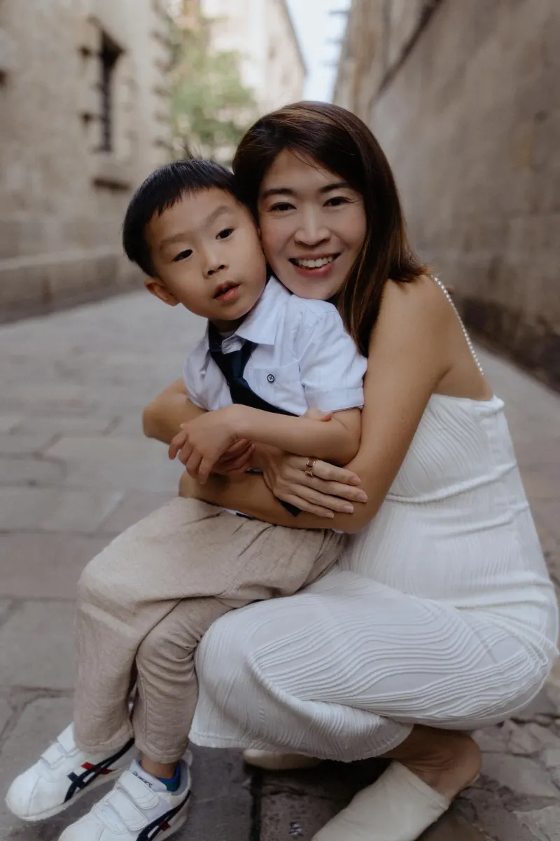 Mother hugs her young son and smiles during a Vacation Portraits photoshoot in a charming Barcelona alleyway.