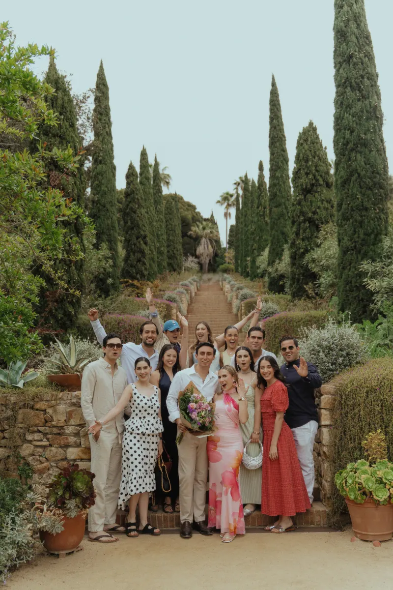 Newly engaged couple celebrates with friends in a lush garden after a surprise proposal photoshoot.
