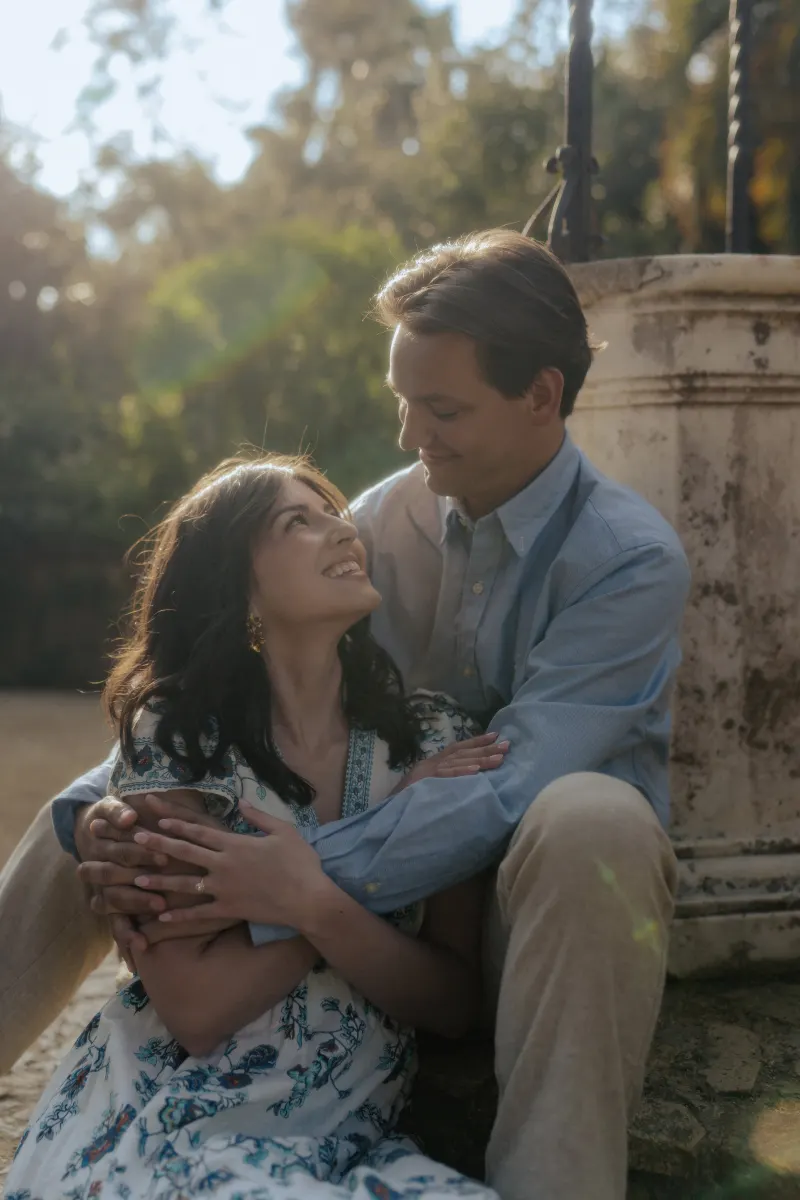 Newly engaged couple embraces and smiles in soft sunlight during a Mediterranean surprise proposal photoshoot.