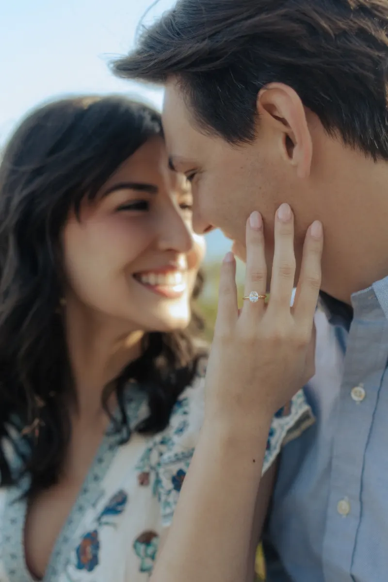 Newly engaged couple shares a joyful embrace, her hand with a sparkling ring highlighted during a surprise proposal photoshoo