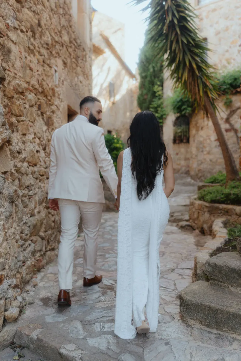 Newly engaged couple strolls hand in hand through a sunlit stone alley during their surprise proposal photoshoot.