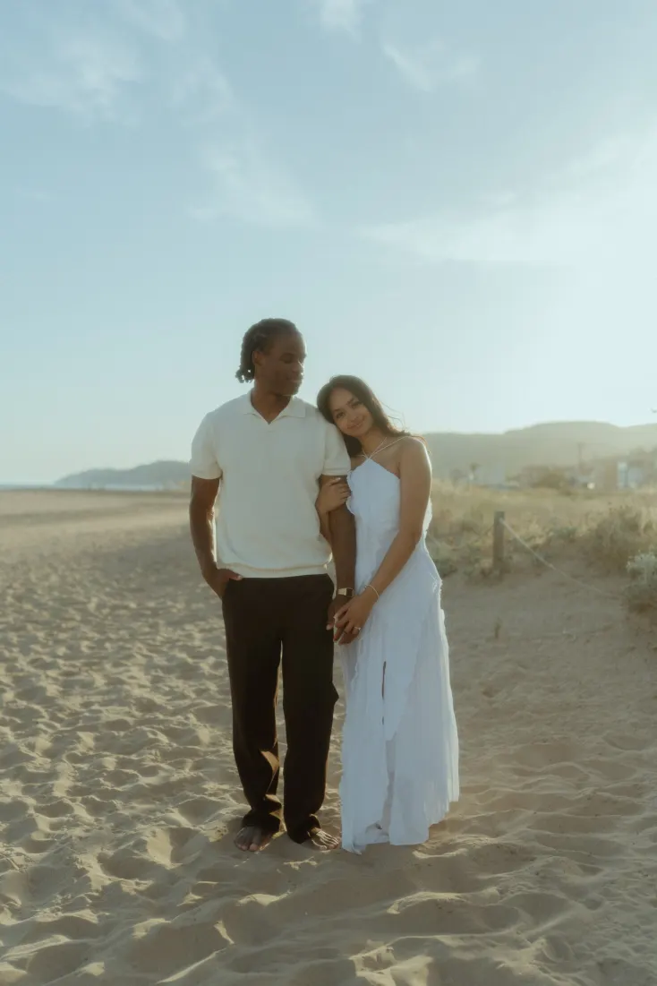 Newly engaged Dexter and Cheryl stand together in warm evening light near the Castelldefels dunes.
