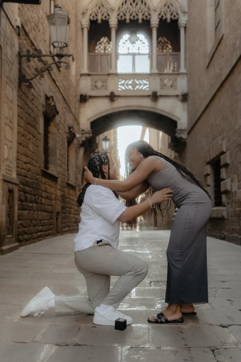 One partner kneels to propose as their loved one embraces them, capturing a joyful surprise proposal in Barcelona’s Gothic Qu