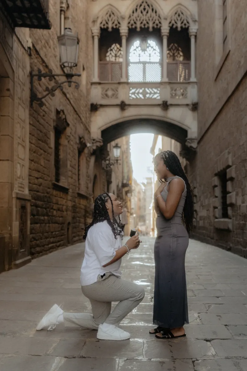 One partner kneels to propose, capturing a joyful surprise proposal moment in Barcelona’s Gothic Quarter.