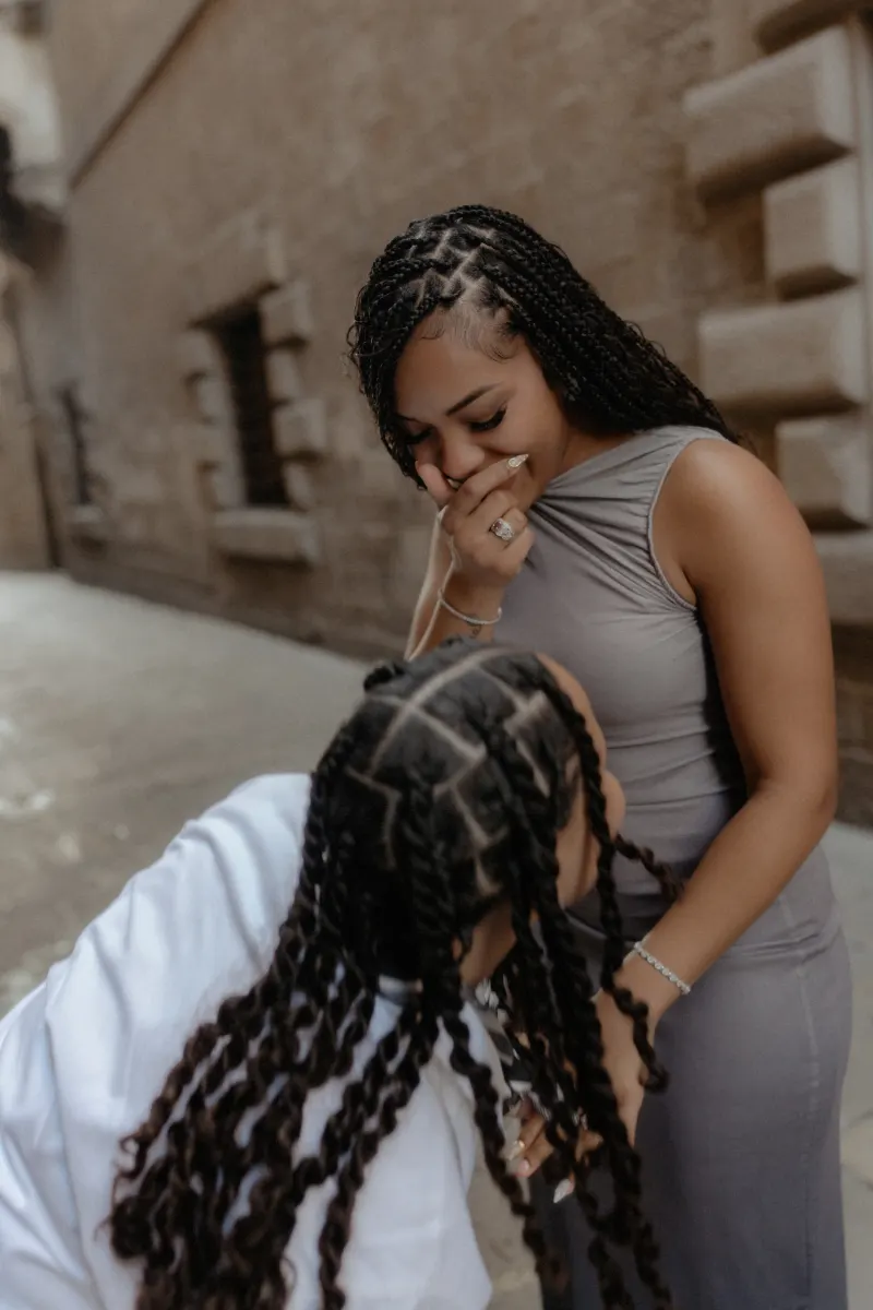 Overjoyed woman covers her mouth in surprise as her partner proposes during a surprise proposal photoshoot in Barcelona.
