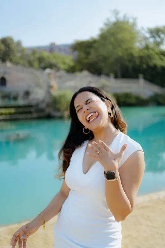 Overjoyed woman shows off her engagement ring and laughs by the water during a surprise proposal photoshoot in Barcelona.