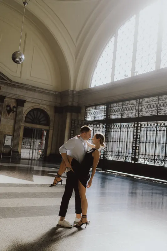 Playful couple dancing together in a sunlit grand hall, celebrating their engagement with a joyful photoshoot moment.