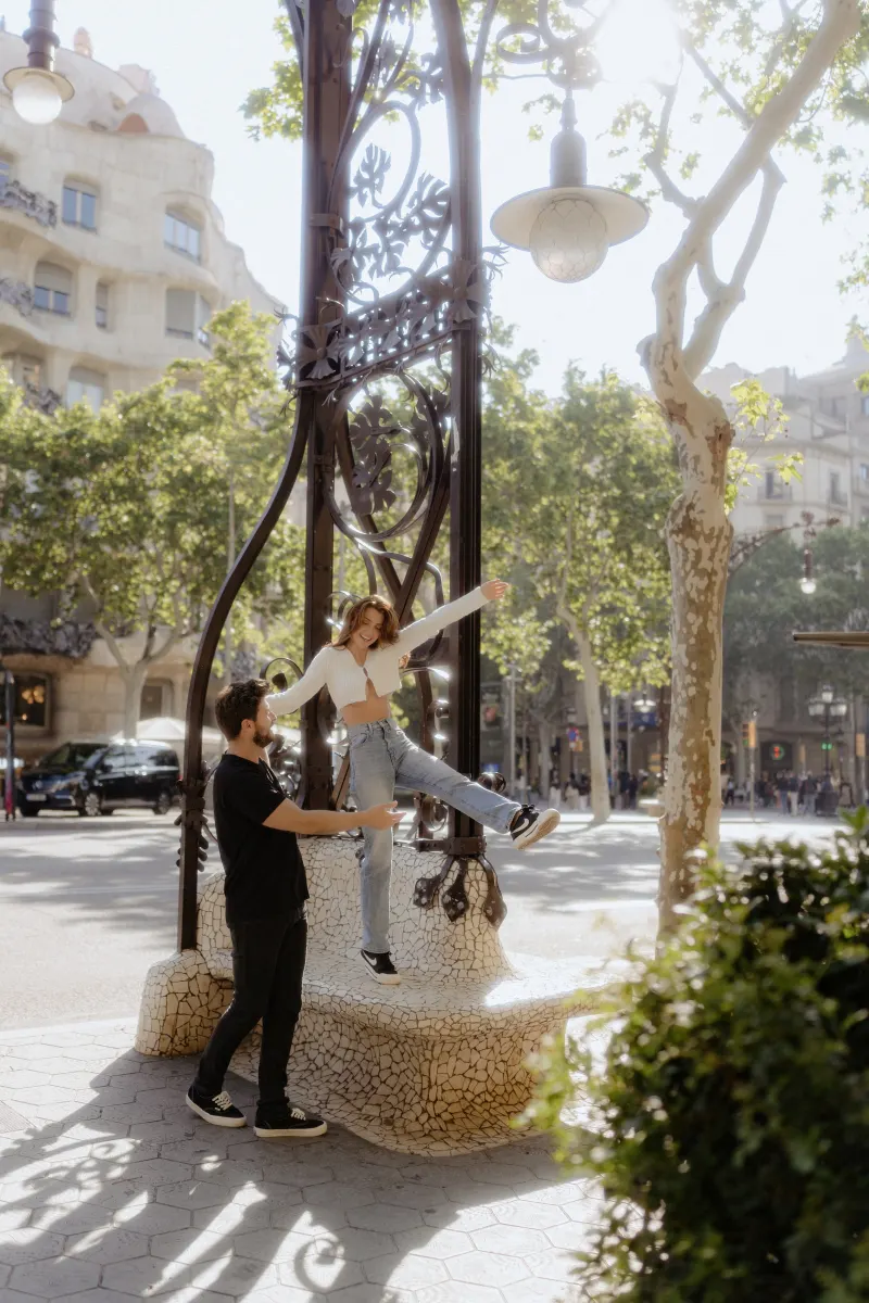 Playful couple enjoys a lighthearted moment on a sunlit city bench during a couples & engagements photoshoot.