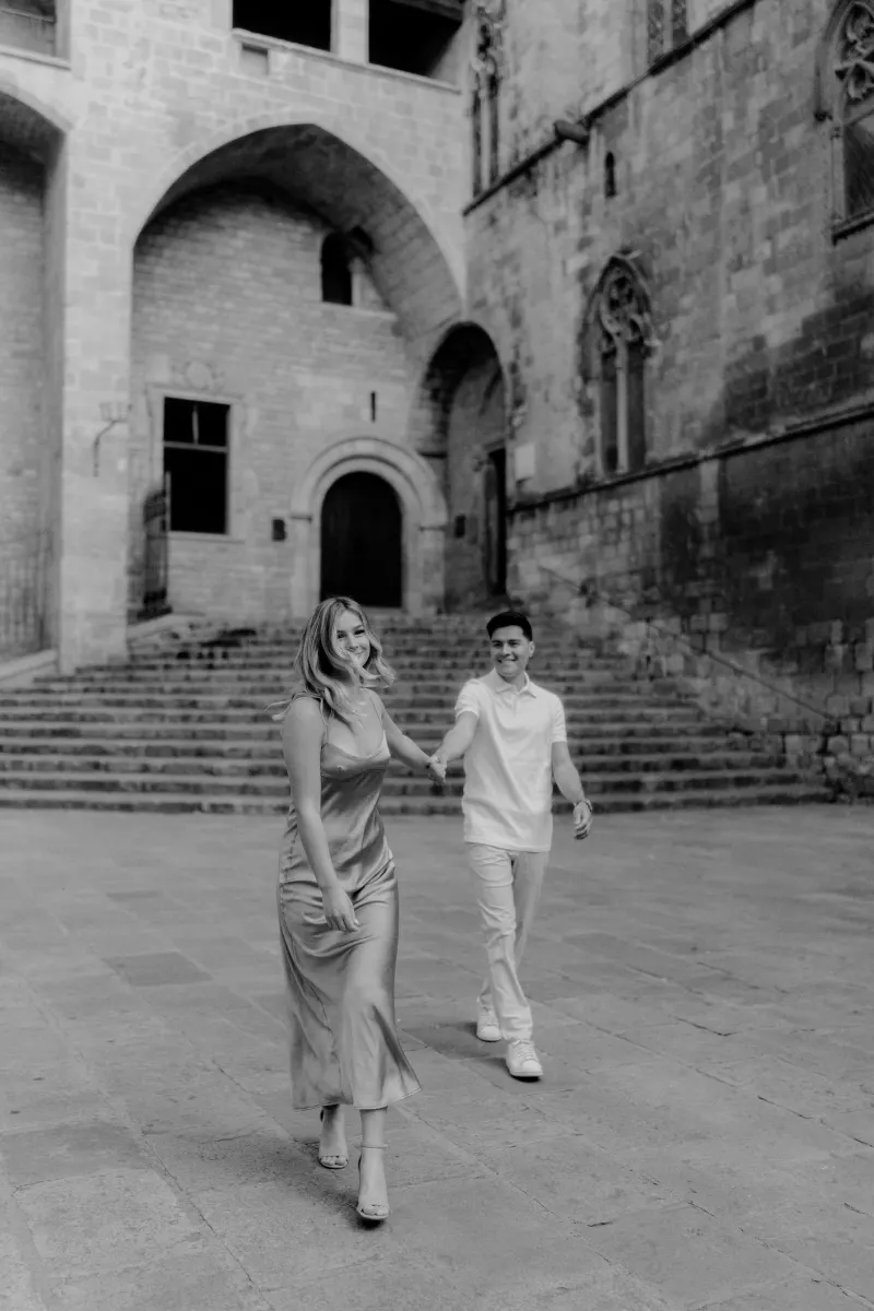 Playful couple holding hands and laughing while exploring historic Barcelona during a Vacation Portraits photoshoot.
