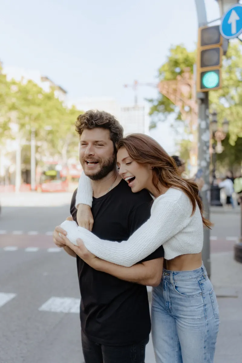 Playful couple shares a joyful hug and laughter on a city street during a couples & engagements photoshoot.