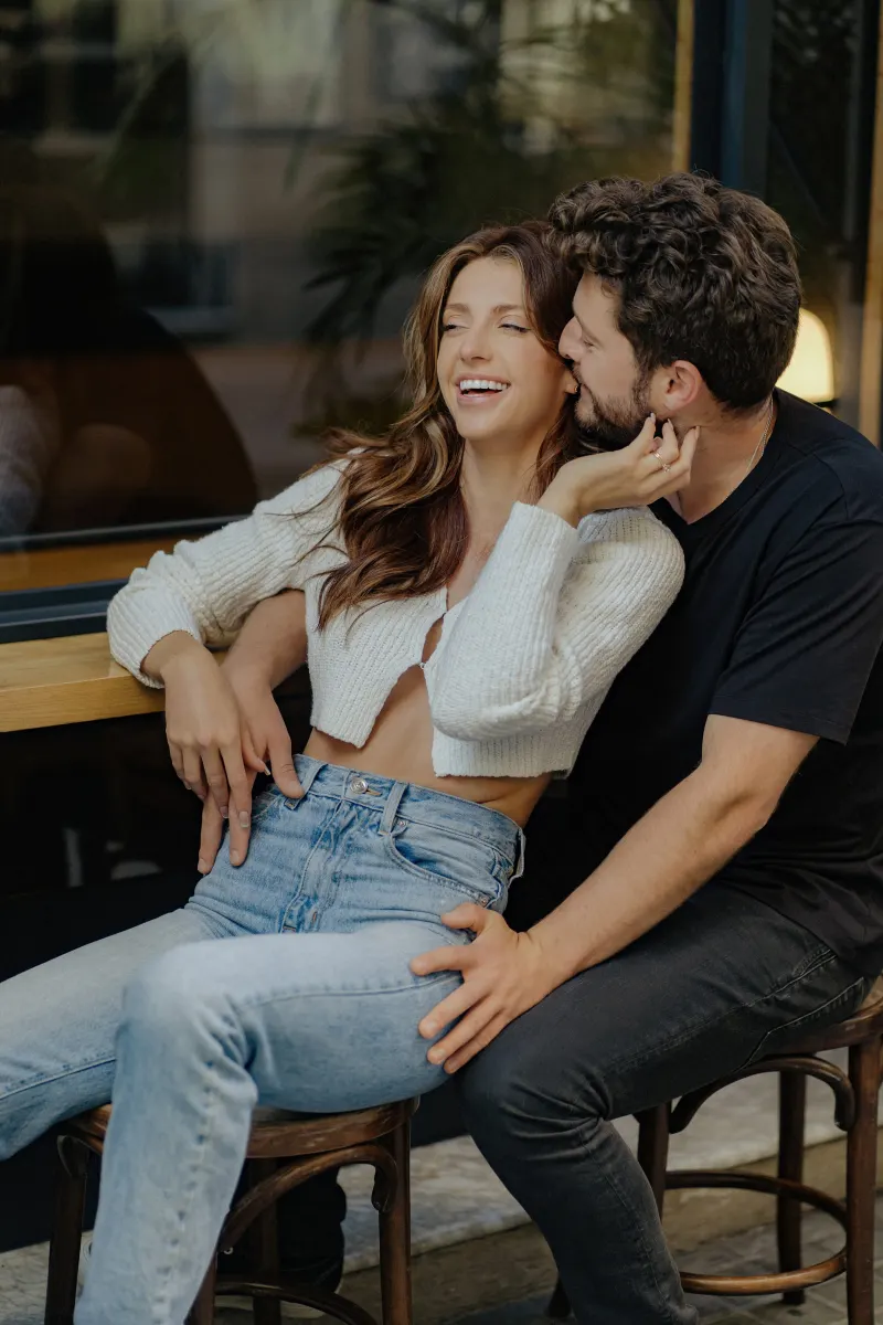 Playful couple shares laughter and a sweet moment at a café during a couples & engagements photoshoot.