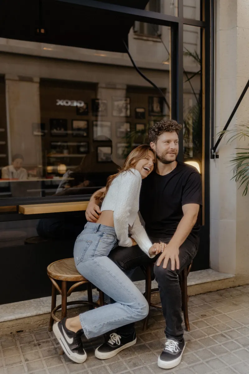 Playful couple shares laughter outside a café, captured during a couples & engagements photoshoot in the city.