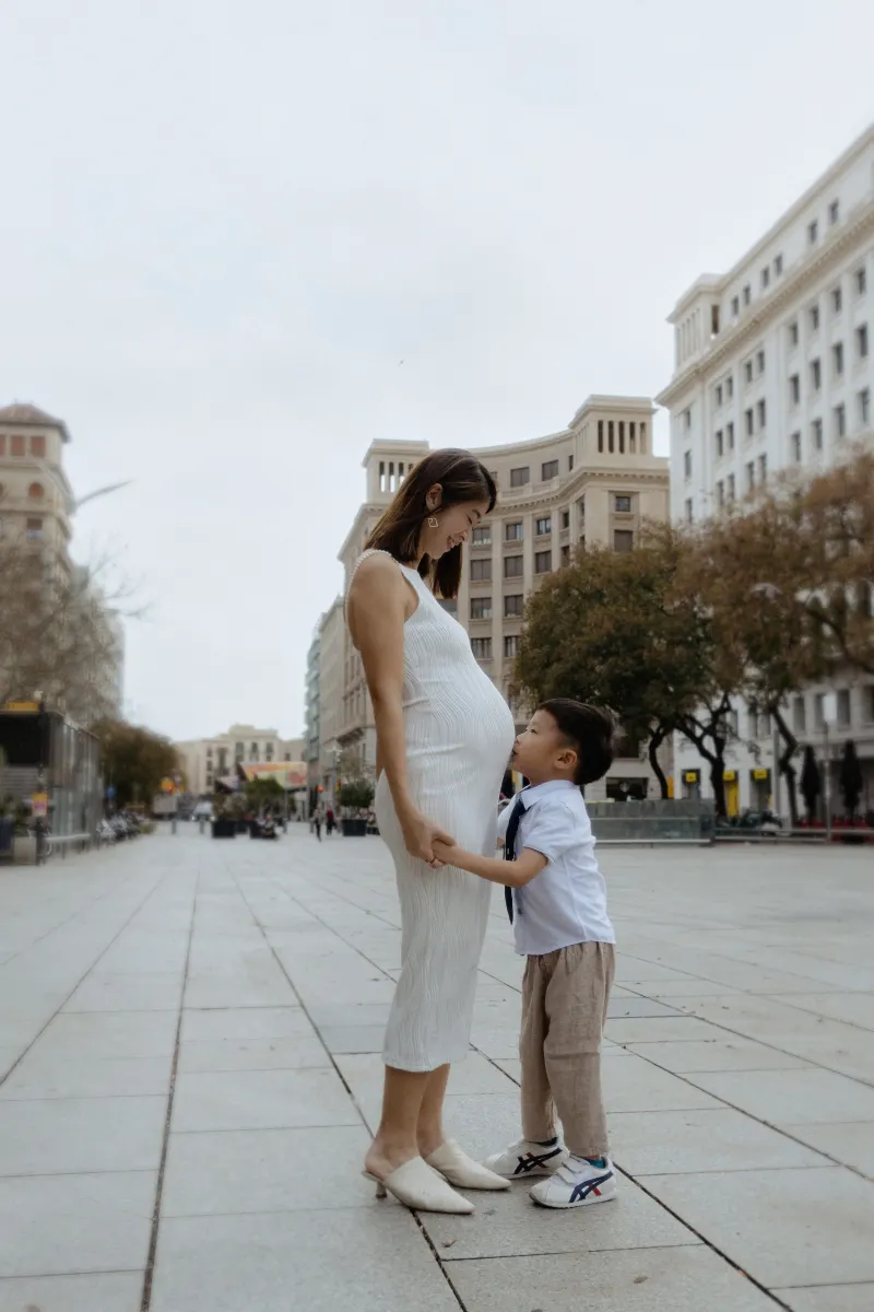 Pregnant mother smiles as her young son hugs her belly during a Vacation Portraits session in a city square.