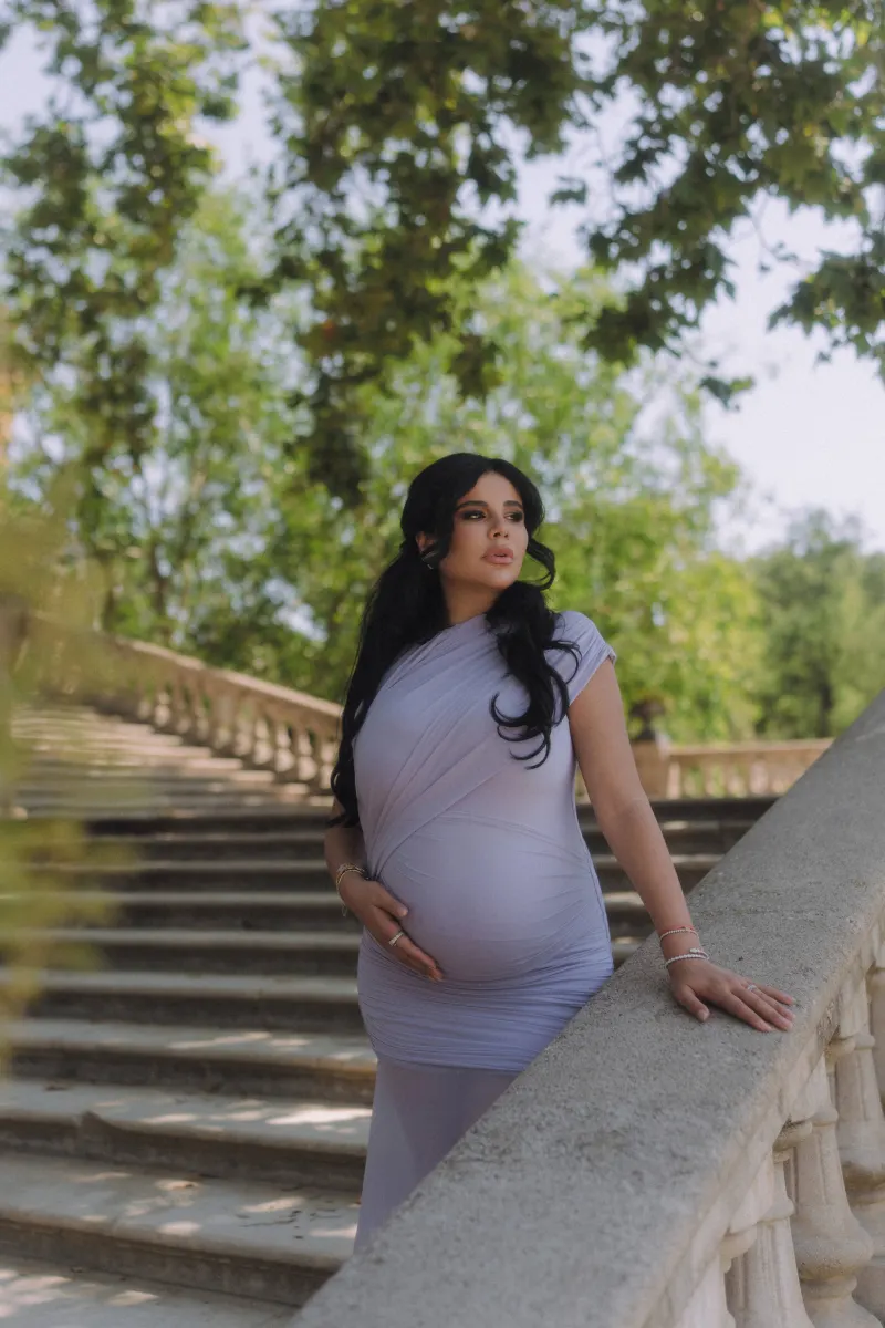 Pregnant woman in a lilac dress gazes thoughtfully on a stone staircase, Vacation Portraits session in Barcelona.