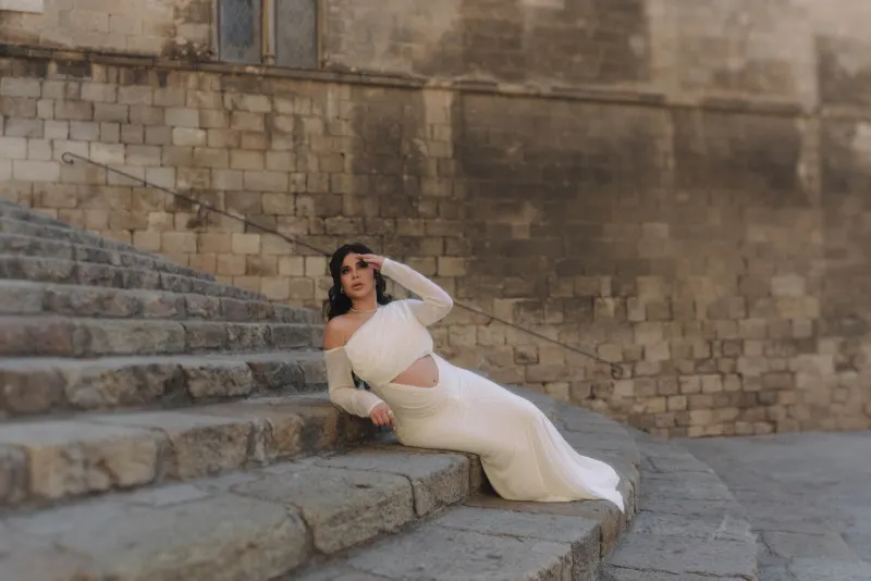 Pregnant woman in a white gown reclines gracefully on historic stone steps during a Vacation Portraits photoshoot.