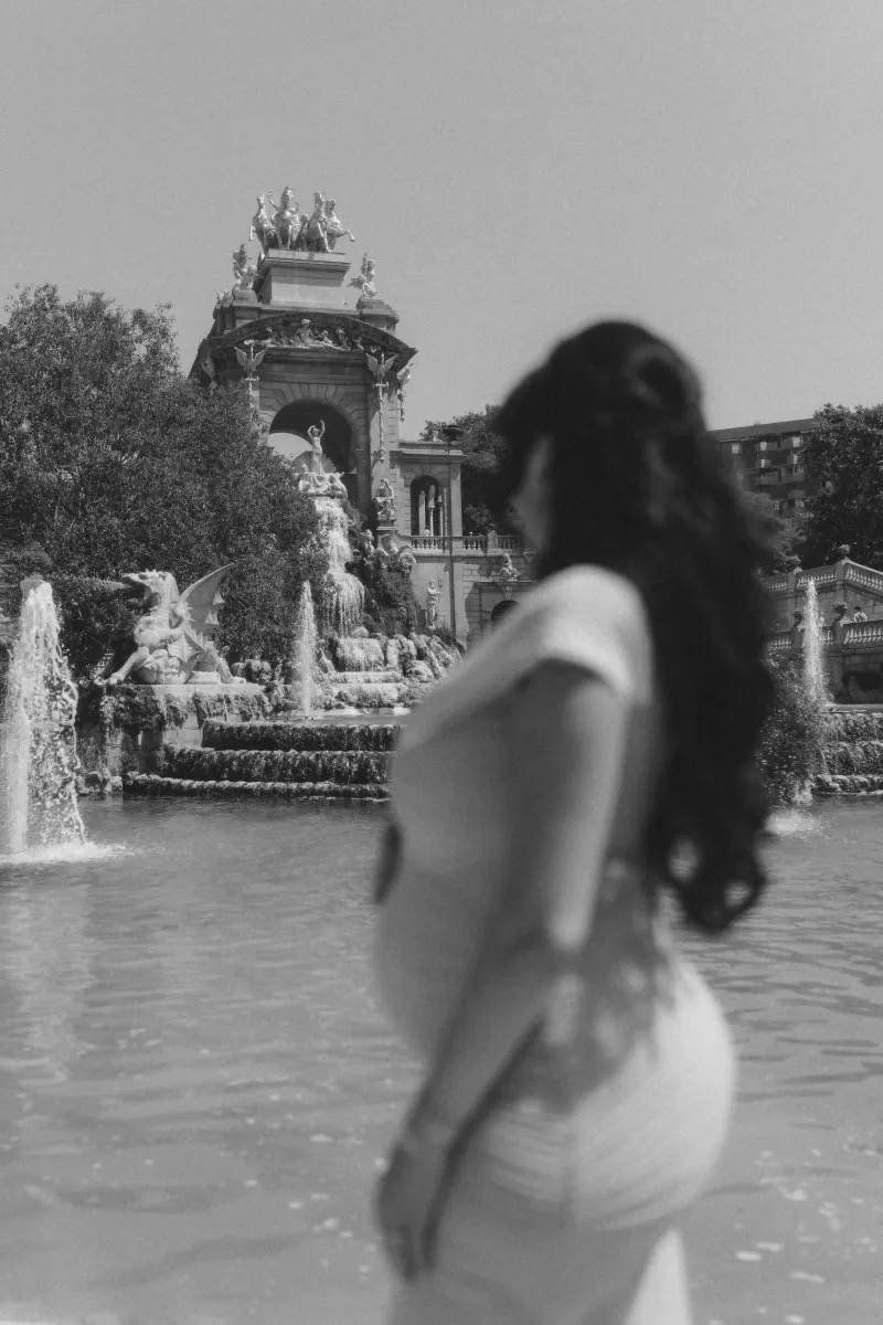 Pregnant woman stands by a grand fountain, Vacation Portraits photoshoot capturing a tranquil moment abroad.