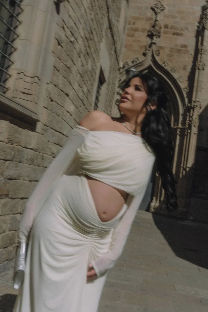 Radiant pregnant woman in a white gown enjoys a Vacation Portraits shoot along sunlit historic stone streets.