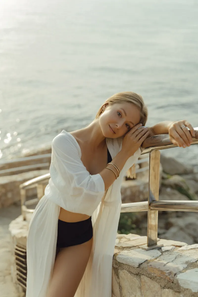 Relaxed woman in swimwear leans on a seaside railing, captured during a Vacation Portraits photoshoot by the water.