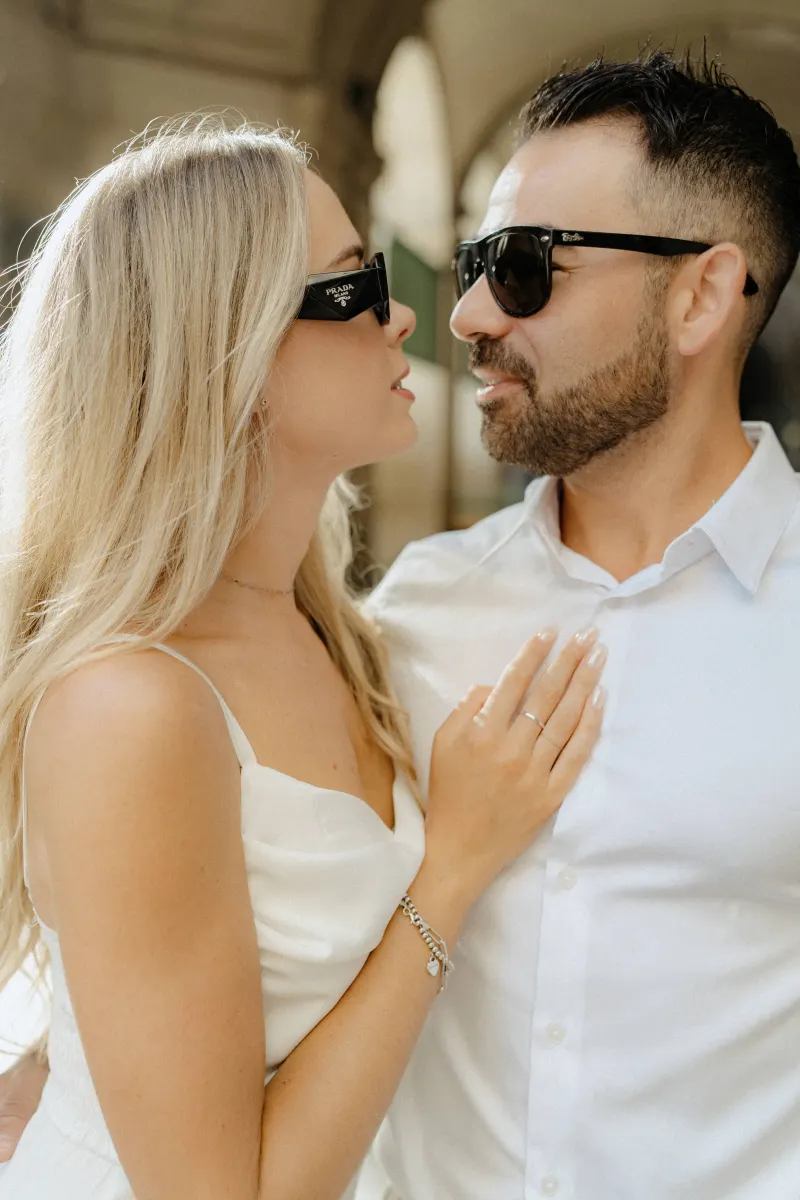 Romantic couple in sunglasses share an intimate moment during a couples & engagements shoot in a sunlit city arcade.