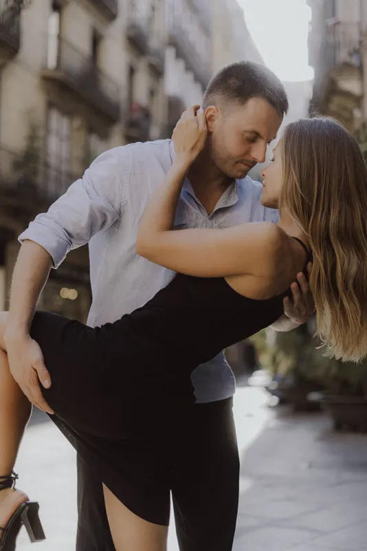 Romantic couple shares a dramatic dip and loving gaze on a sunlit city street during a couples & engagements photoshoot.